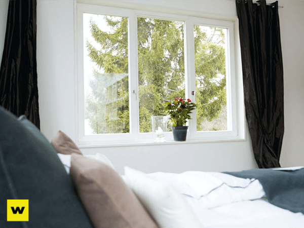 Modernes Schlafzimmer mit großem Fenster, Pflanzen und Blick ins Grüne für wohnliche Atmosphäre.