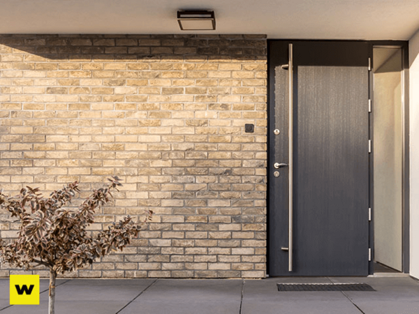 Moderne Haustür aus dunklem Aluminium mit Glaseinsatz vor heller Klinkerfassade.